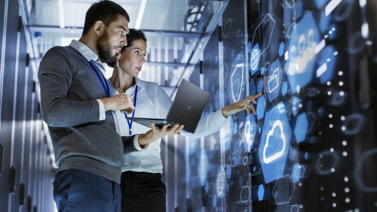 Male IT Specialist Holds Laptop and Discusses Work with Female Server Technician. They’re Standing in Data Center, Rack Server Cabinet with Cloud Server Icon and Visualization.