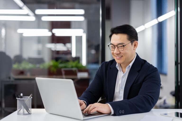 Asian man in business suit and glasses working with laptop inside office, mature businessman typing on keyboard, preparing financial report, male company employee at workplace